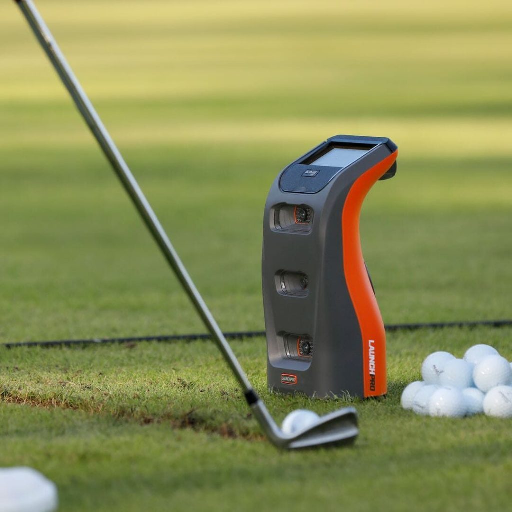 Bushnell Launch Pro beside a golf ball as an iron strikes it