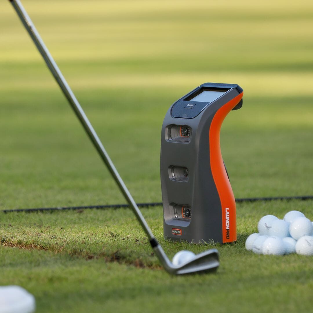 Bushnell Launch Pro beside a golf ball as an iron strikes it