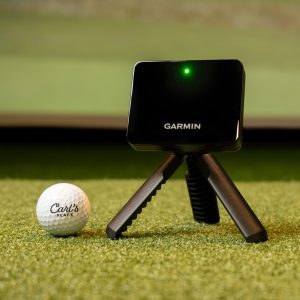 Garmin Approach R10 launch monitor on its tripod behind a golf ball on turf