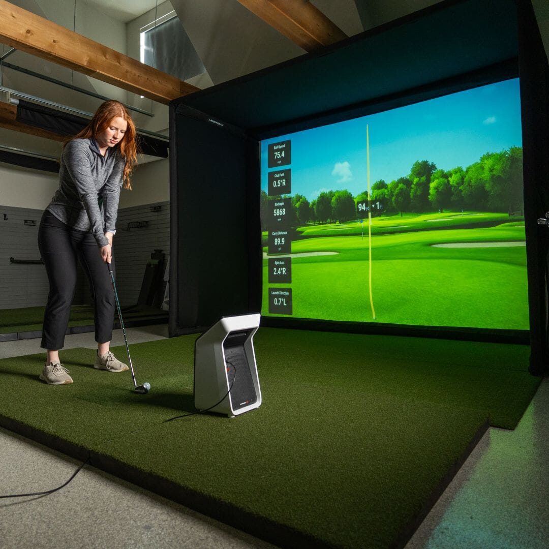 A golfer hitting from a mat into a home simulator screen