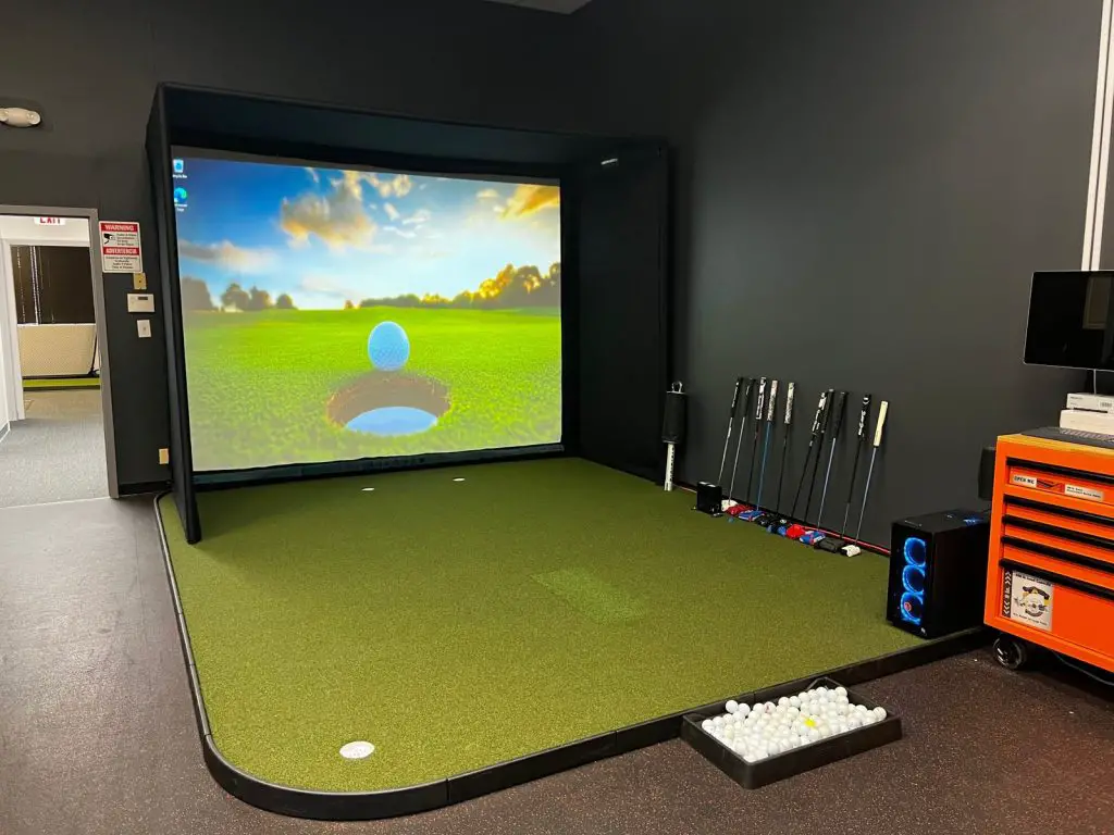 Golf Simulator Flooring (2026): What Goes Under and Around the Mat 4 SIGPRO Golf Simulator Flooring with a hitting strip and putting cups in a simulator room
