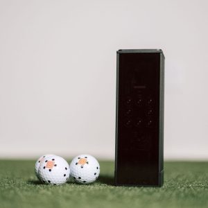 Square Golf Home Edition launch monitor on turf next to two marked golf balls