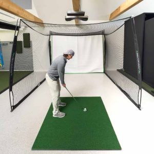 A golfer hitting into a 10 by 8 by 10 ft Square Golf net from a mat