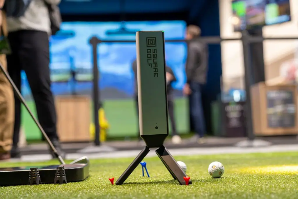 Square Golf Omni launch monitor on a tripod beside the ball in a simulator bay